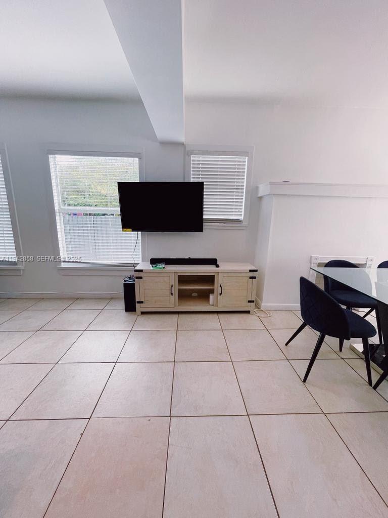 A living room features light-colored tile flooring, a wall-mounted television, and a wooden media console — 105 NW 31st St # 1, Miami FL 33127, MIAMI, FL