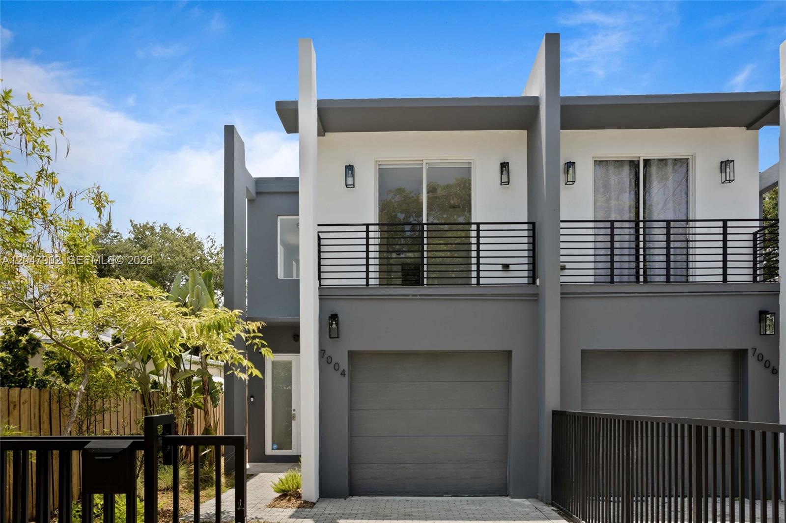 A modern two-story townhouse features a gray garage, a balcony, and a white front door — 7004 NE 5th Ave, Miami FL 33138, MIAMI, FL