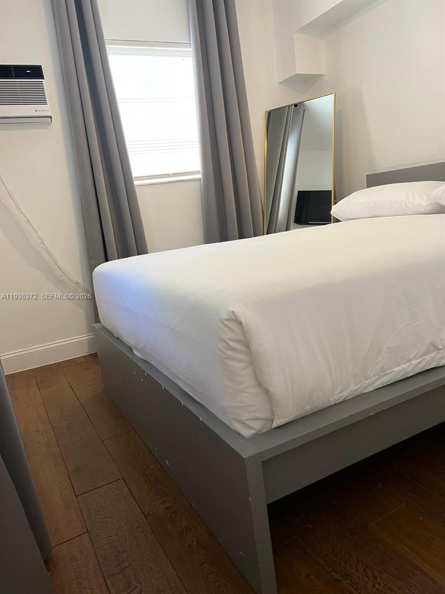 A bedroom features a gray bed frame, white bedding, a window with curtains, and a mirror — 740 Michigan Ave # 5, Miami Beach FL 33139, MIAMI BEACH, FL