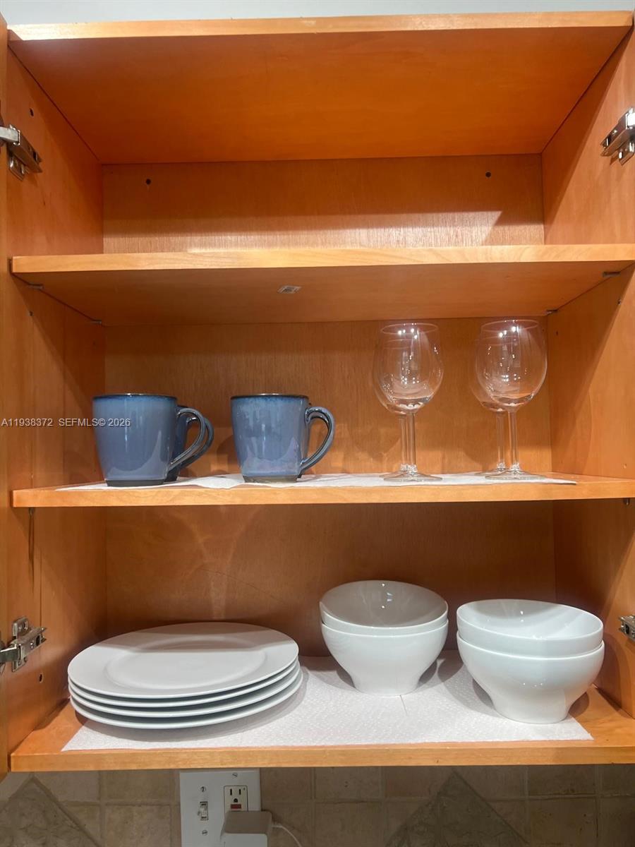 An open wooden kitchen cabinet contains mugs, wine glasses, plates, and bowls — 740 Michigan Ave # 5, Miami Beach FL 33139, MIAMI BEACH, FL