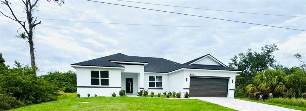 A single-story white house with a dark roof and a two-car garage sits on grass — 14358 MCFARLAND AVENUE, PORT CHARLOTTE, FL