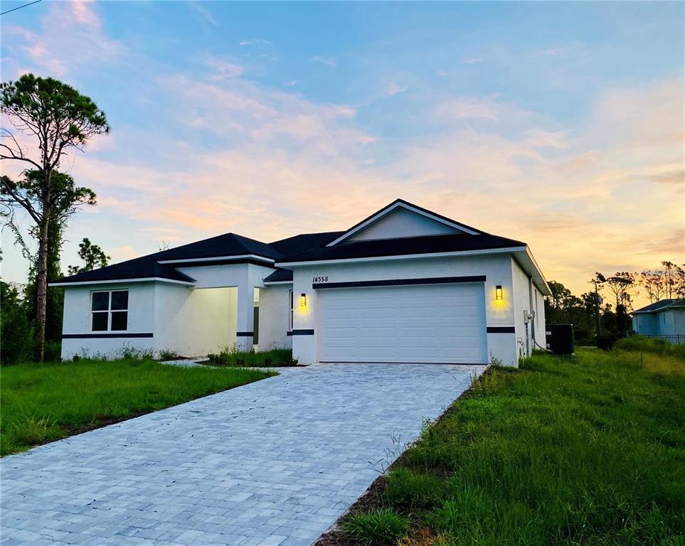 A white single-story house with a two-car garage and a paved driveway at sunset — 14358 MCFARLAND AVENUE, PORT CHARLOTTE, FL