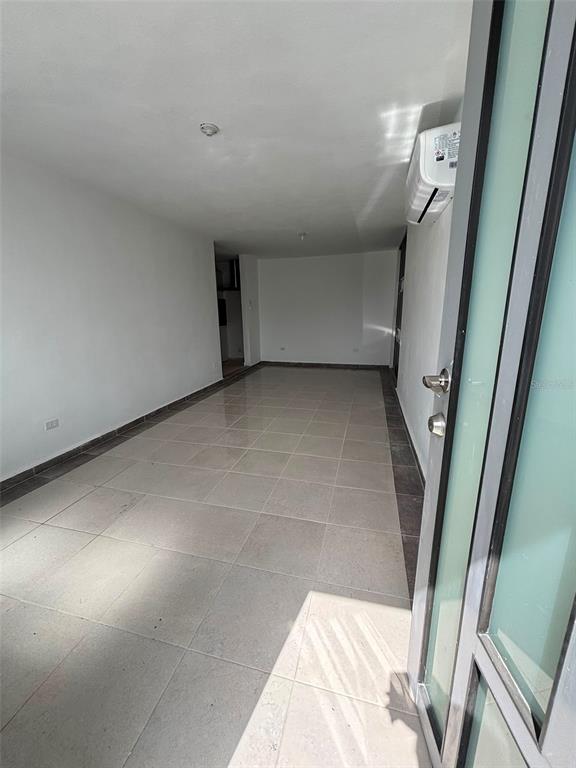 An empty room with light-colored tile flooring, white walls, and a wall-mounted air conditioner — 18-6 18 Street SABANA GARDENS, CAROLINA, PR