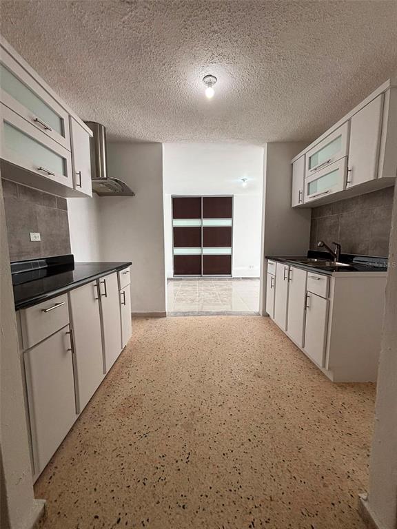 A galley kitchen features white cabinets, black countertops, and light-colored speckled flooring — 18-6 18 Street SABANA GARDENS, CAROLINA, PR