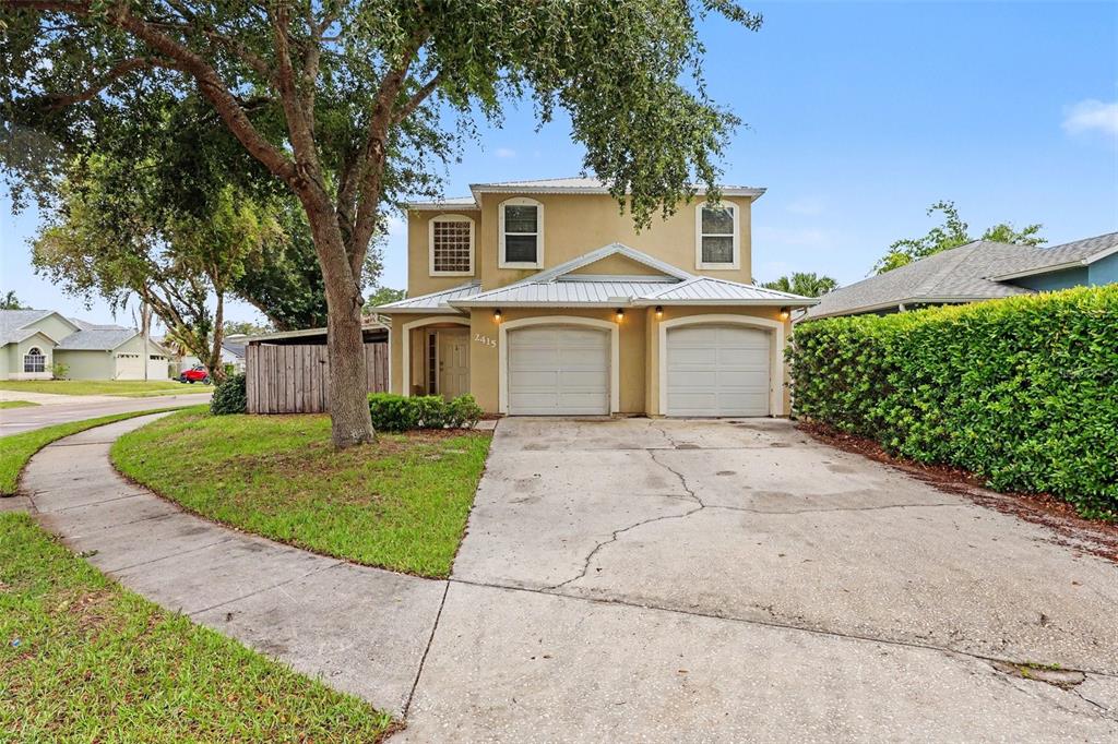 A two-story house with a tan stucco exterior, two garage doors, and a concrete driveway — 2415 SAINT PAULS DRIVE, TITUSVILLE, FL