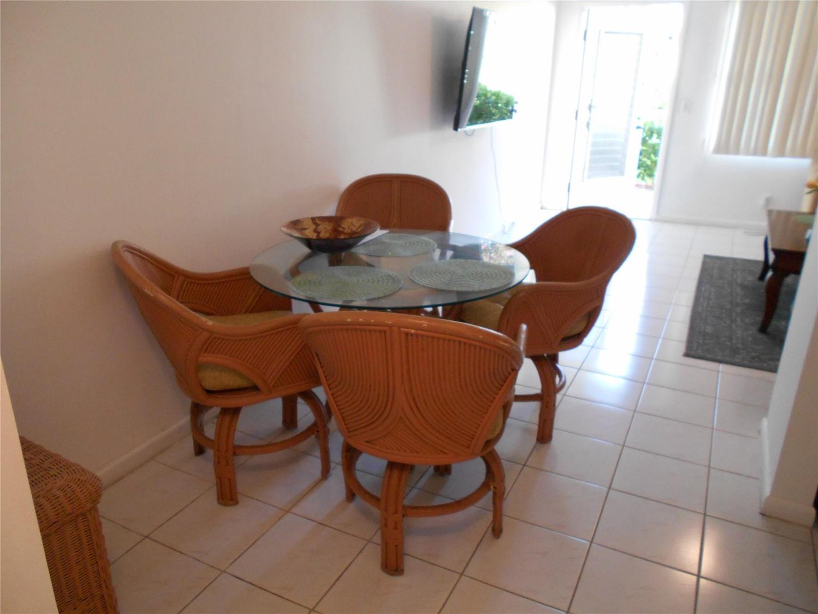 A dining area features a glass-topped table with four wicker chairs on a tiled floor — 91 Preston C # 91, Boca Raton FL 33434, BOCA RATON, FL