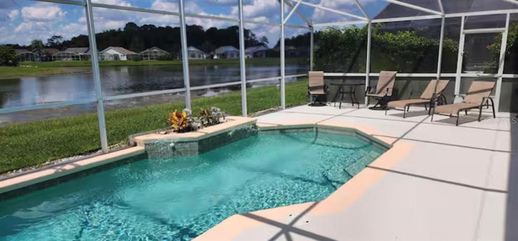 A screened-in pool patio overlooks a lake with lounge chairs and a small water feature — 622 EAGLE POINTE S, KISSIMMEE, FL