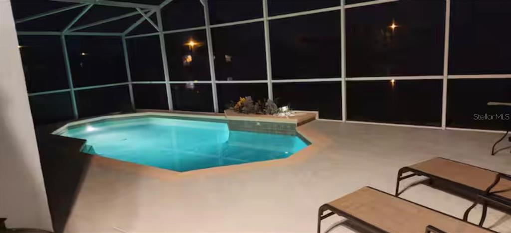 A screened-in lanai features a lit swimming pool and two lounge chairs at night — 622 EAGLE POINTE S, KISSIMMEE, FL