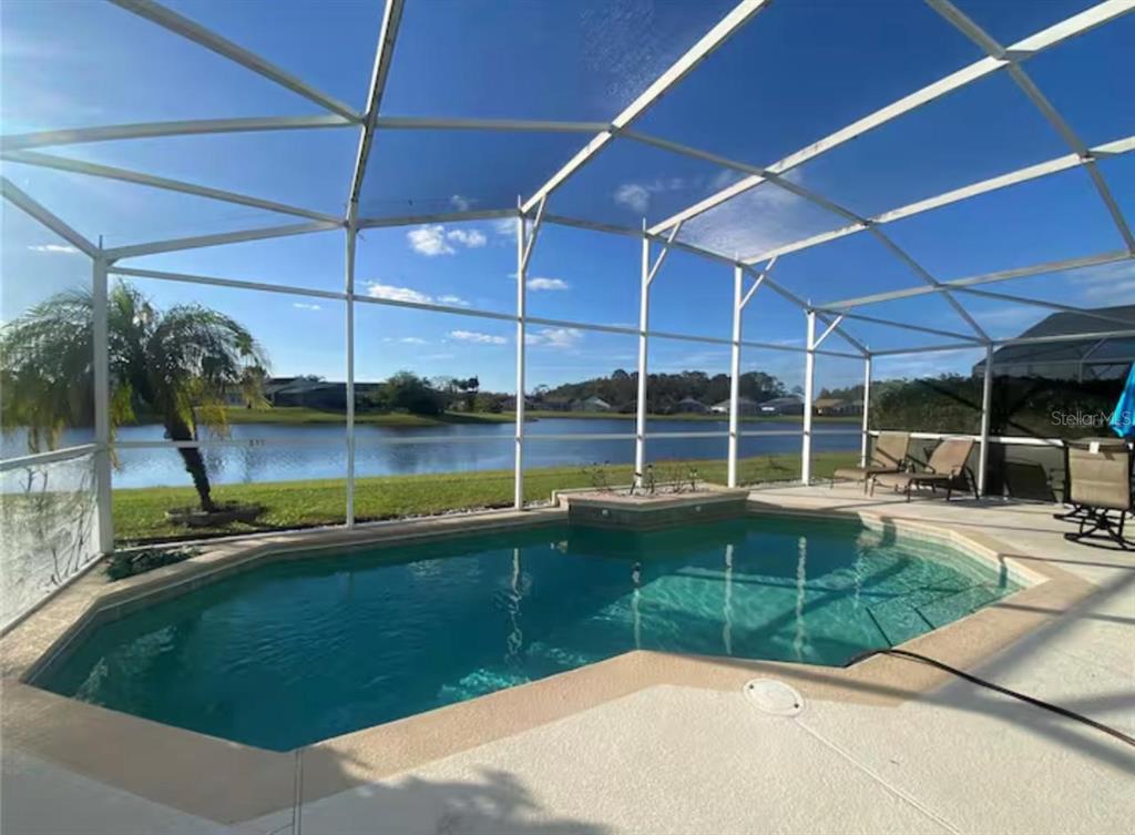 A screened-in swimming pool overlooks a lake with a palm tree and lounge chairs — 622 EAGLE POINTE S, KISSIMMEE, FL