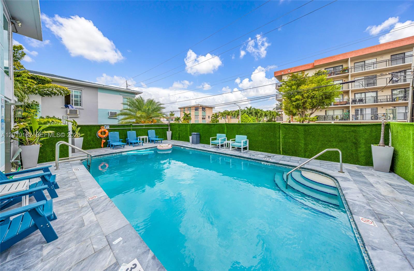 An outdoor swimming pool with blue lounge chairs is surrounded by a green privacy fence — 7830 Abbott Ave, Miami Beach FL 33141, MIAMI BEACH, FL