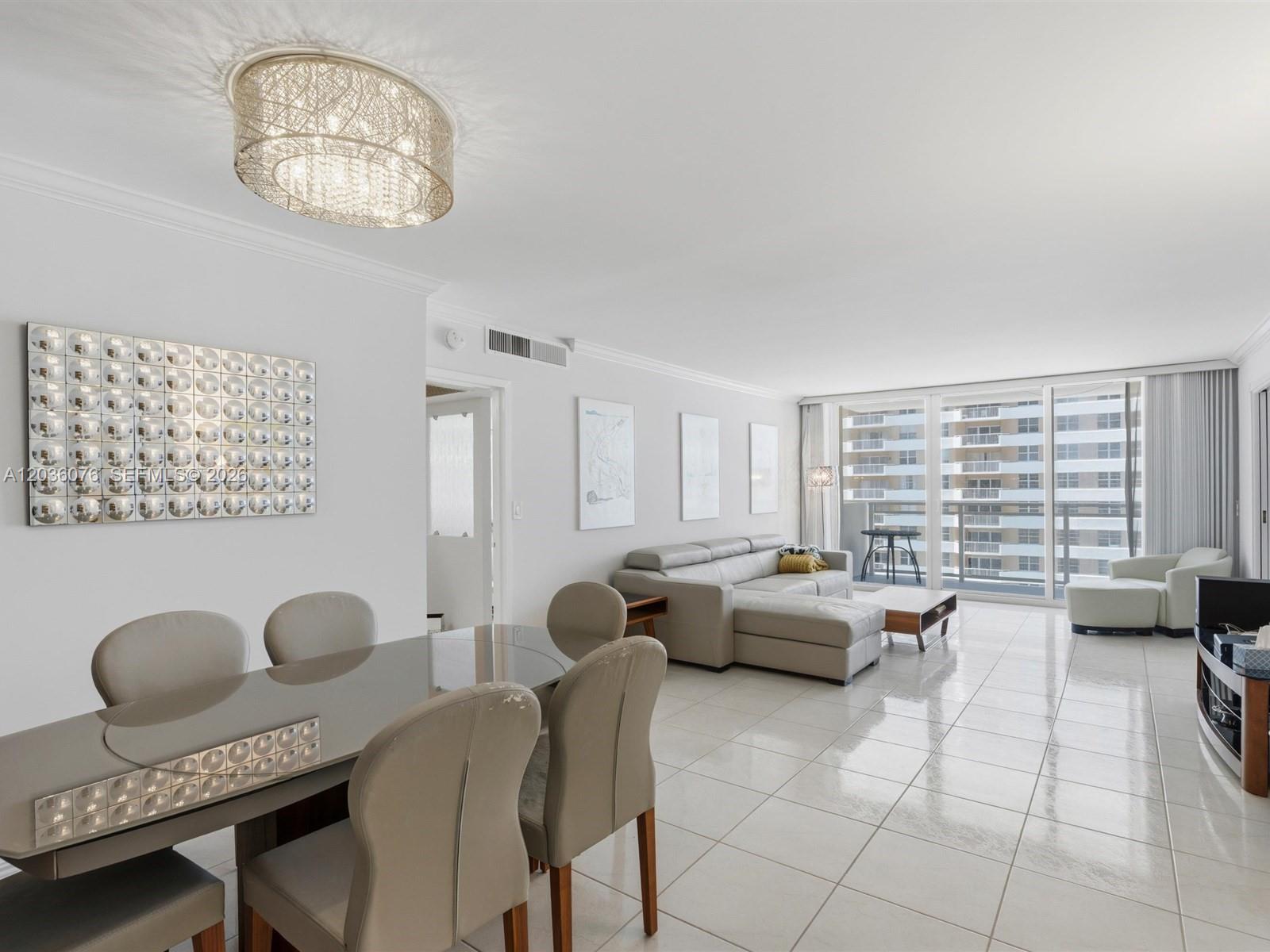 A bright, open-concept living and dining area features white tile floors and a modern chandelier — 2030 S Ocean Dr # 1123, Hallandale Beach FL 33009, HALLANDALE BEACH, FL
