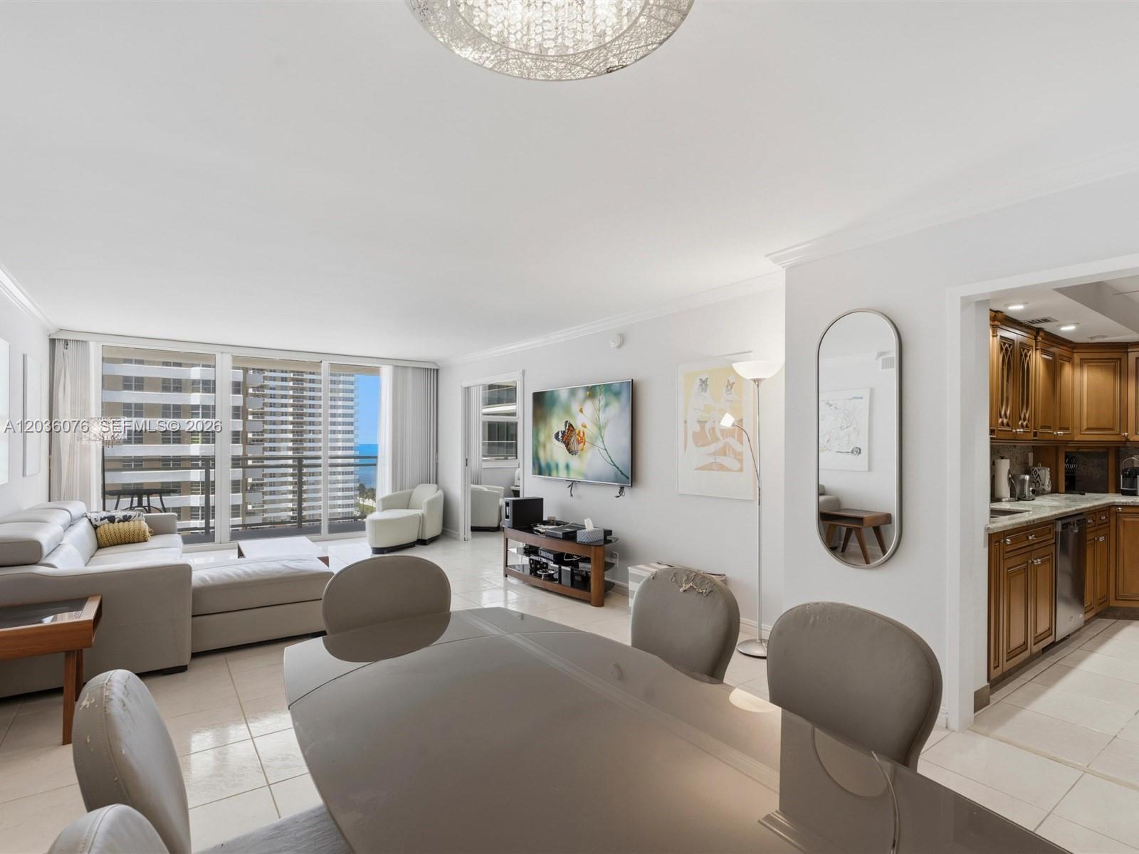 A living and dining area with a grey sectional, glass table, and adjacent wooden kitchen — 2030 S Ocean Dr # 1123, Hallandale Beach FL 33009, HALLANDALE BEACH, FL
