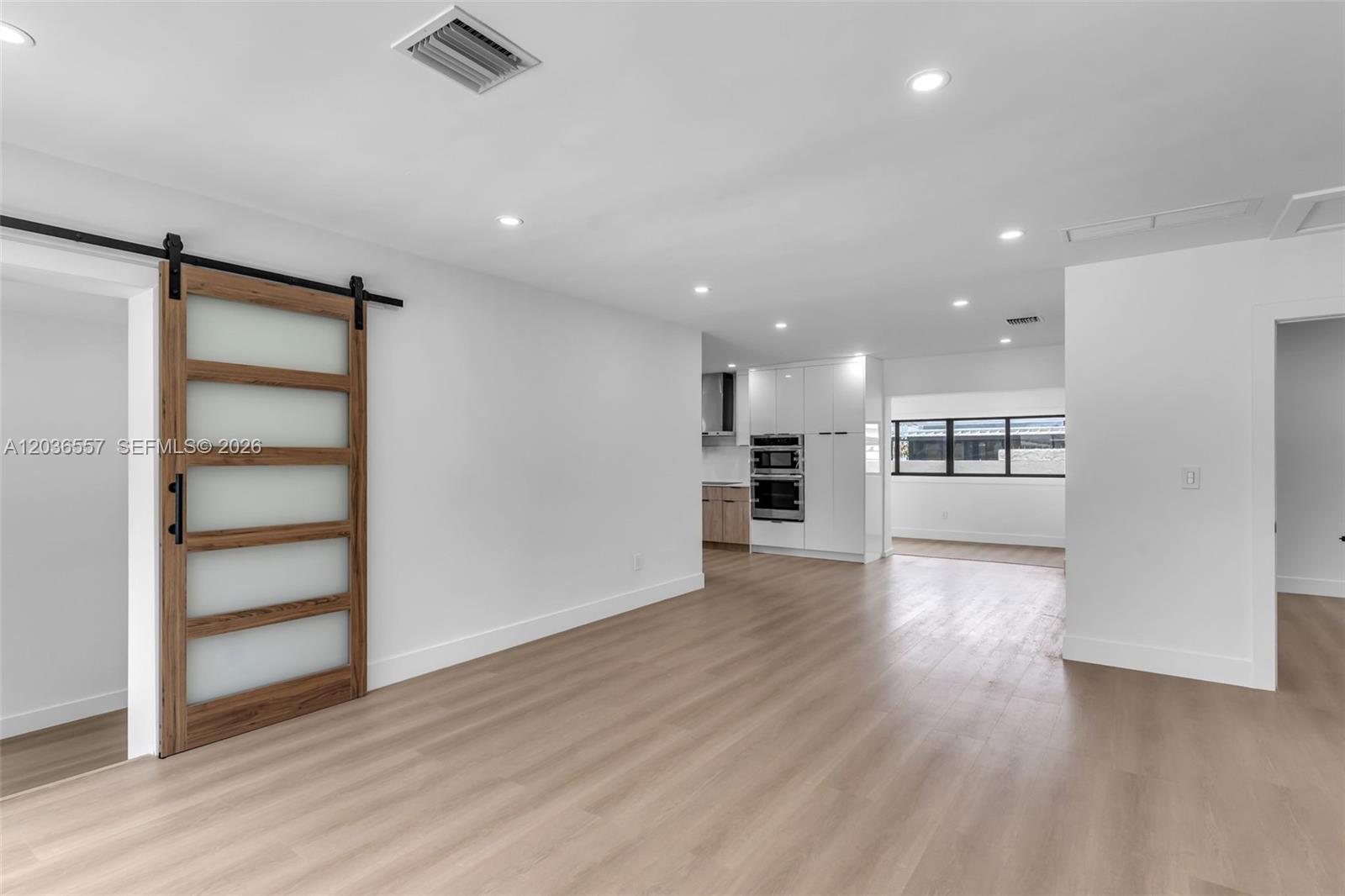 A bright room with light wood flooring, a sliding barn door, and a modern kitchen — 4353 SW 2nd St, Miami FL 33134, MIAMI, FL