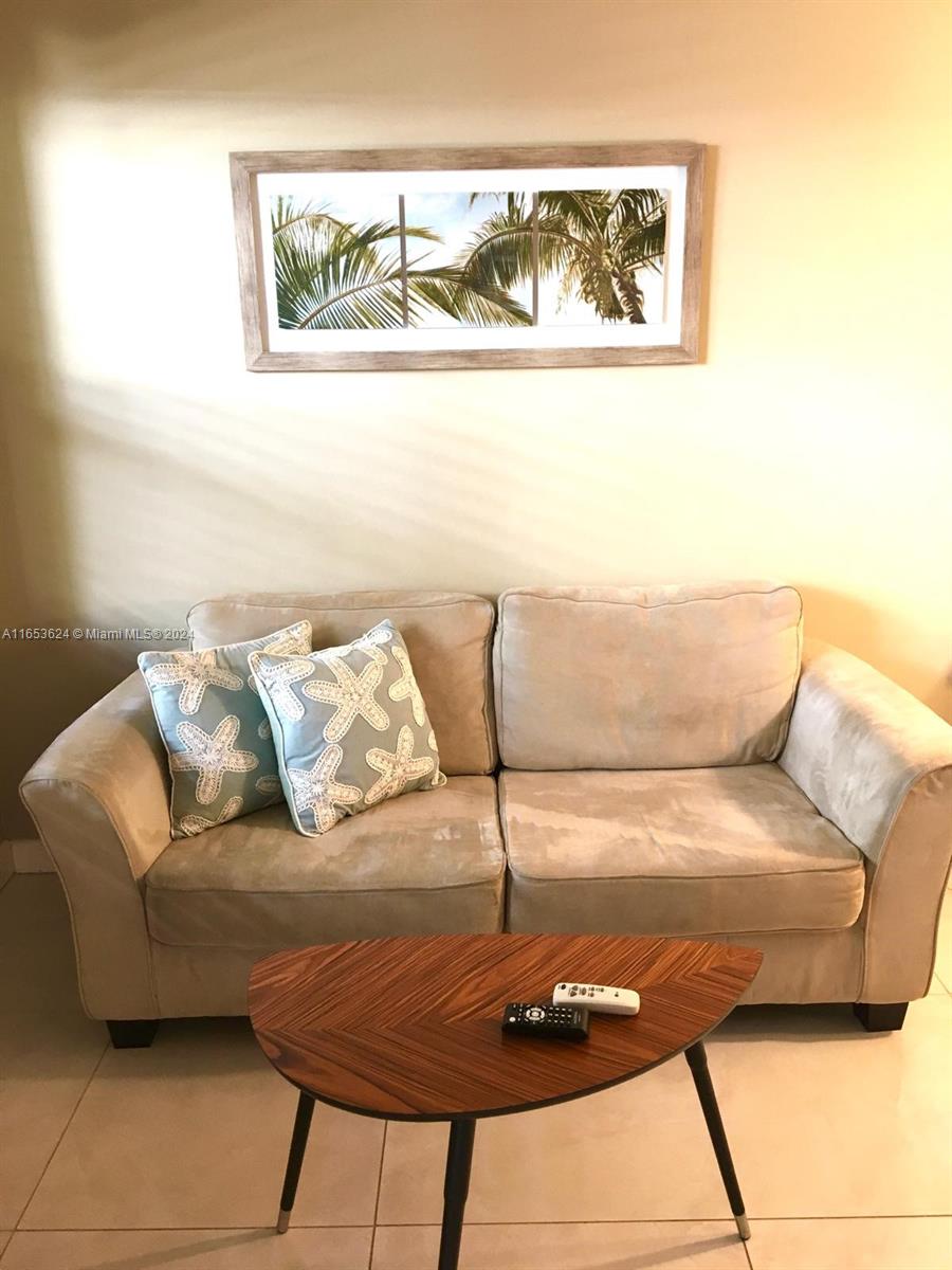 A beige sofa with two starfish-patterned pillows sits in front of a palm tree print — 1228 Pennsylvania Ave # 2, Miami Beach FL 33139, MIAMI BEACH, FL