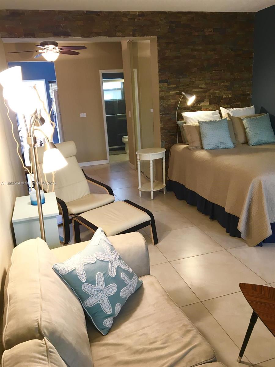 A bedroom features a stone accent wall, a bed, a lounge chair, and tiled floors — 1228 Pennsylvania Ave # 2, Miami Beach FL 33139, MIAMI BEACH, FL