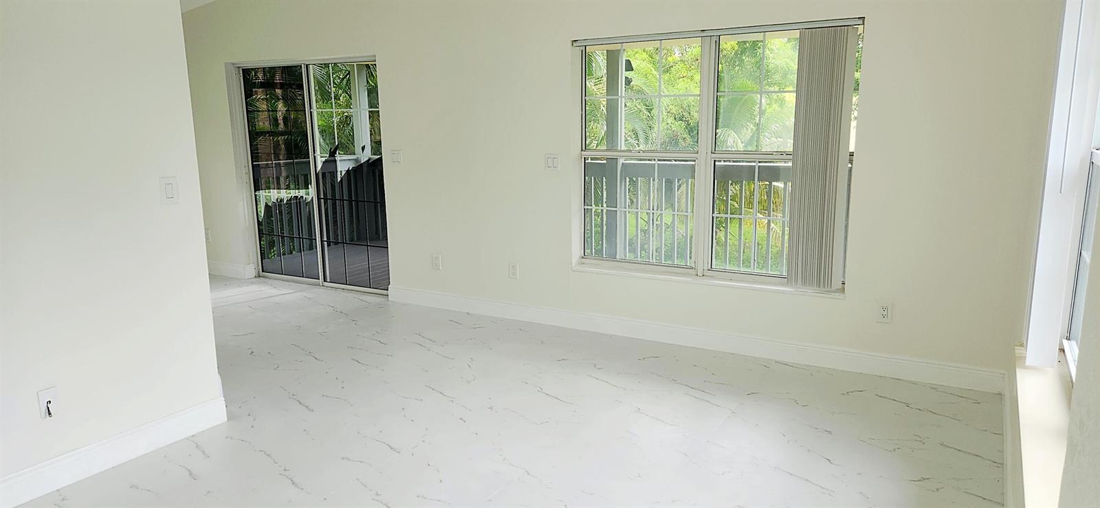 An empty room with white marble-look tile flooring, a sliding glass door, and large windows — 11128 N 59th St Street N, FL 33411, FL