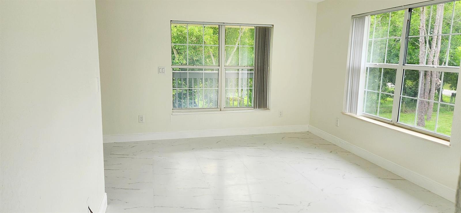 An empty room with white marble-look tile flooring and two large windows overlooking trees — 11128 N 59th St Street N, FL 33411, FL