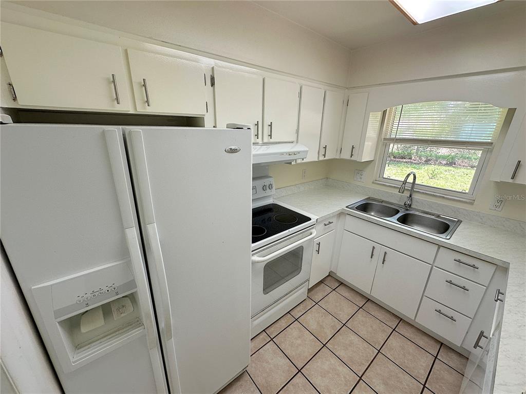 A kitchen with white cabinets, white appliances, a double sink, and tiled flooring — 4146 NW 30TH TERRACE, GAINESVILLE, FL