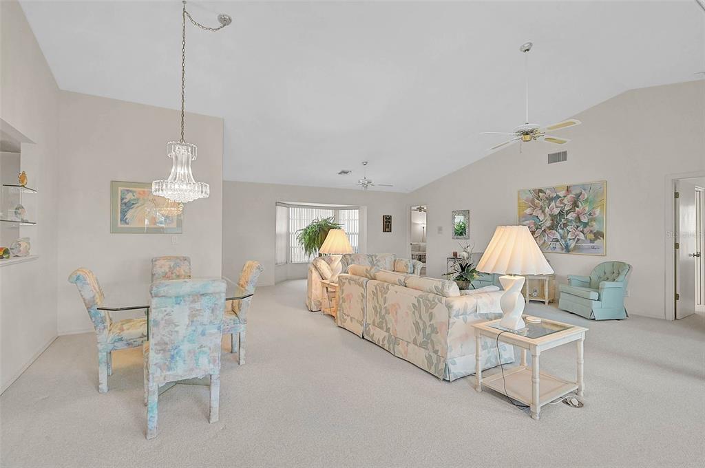 A living and dining room with light-colored carpet, floral furniture, and a crystal chandelier — 4360 PRESIDENTIAL AVENUE CIRCLE E, BRADENTON, FL