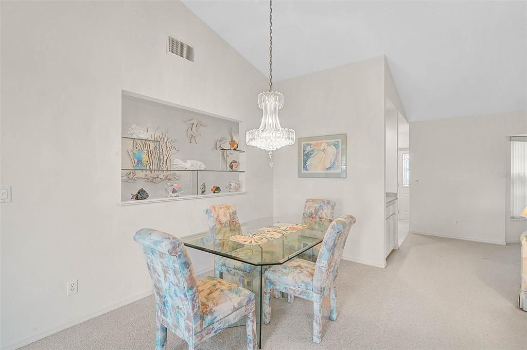 A dining room features a glass-top table, floral chairs, a crystal chandelier, and a wall niche — 4360 PRESIDENTIAL AVENUE CIRCLE E, BRADENTON, FL