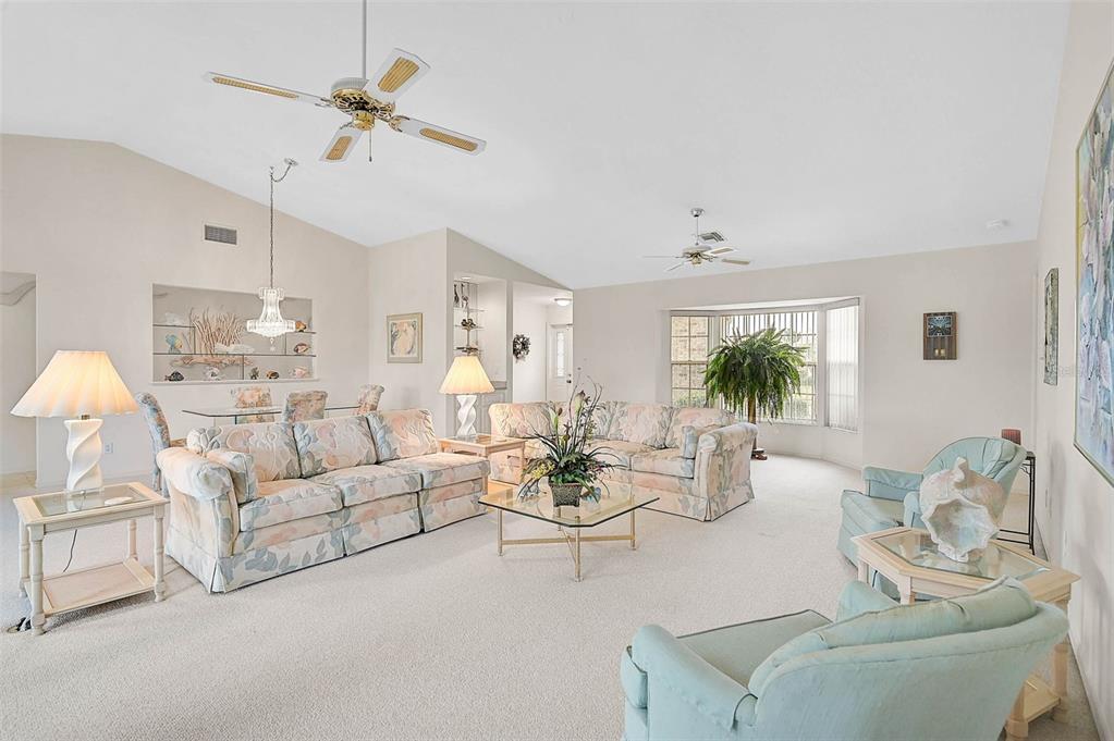A spacious living room with floral sofas, light carpeting, vaulted ceilings, and a dining area — 4360 PRESIDENTIAL AVENUE CIRCLE E, BRADENTON, FL
