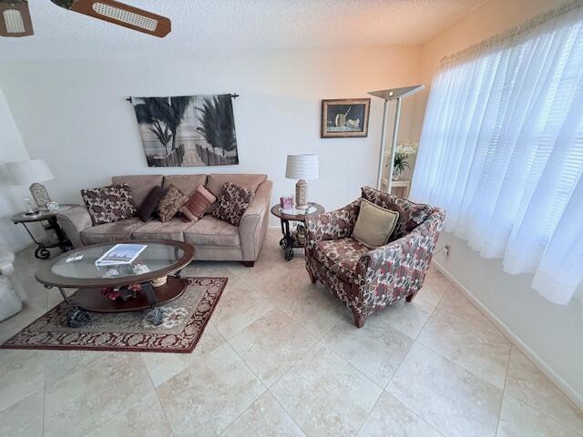 A living room features a beige sofa, patterned armchair, glass coffee table, and tiled floors — 174 Prescott I, Deerfield Beach FL 33442, DEERFIELD BEACH, FL