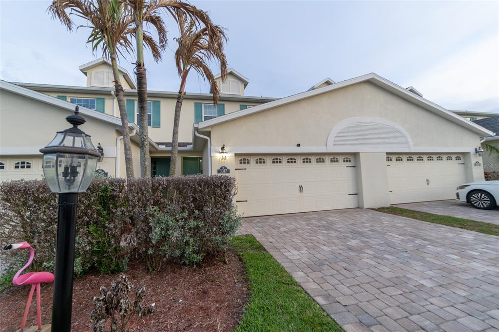 A beige two-story townhouse features a paver driveway, two garage doors, and palm trees — 1017 STEVEN PATRICK AVENUE, INDIAN HARBOUR BEACH, FL
