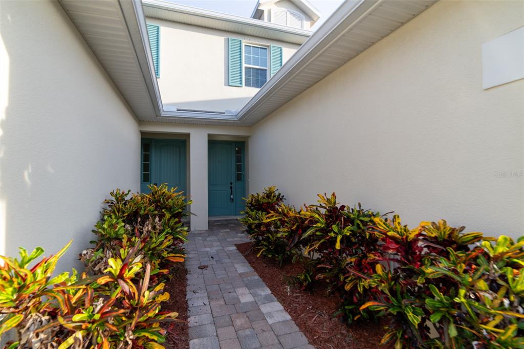 A covered entryway features two teal front doors and paver flooring flanked by colorful plants — 1017 STEVEN PATRICK AVENUE, INDIAN HARBOUR BEACH, FL