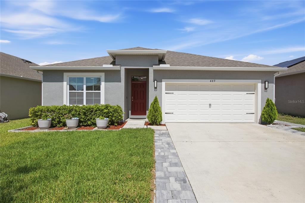 A single-story house with a gray stucco exterior, a red front door, and a two-car garage — 489 LADY GRACE PLACE, DELAND, FL