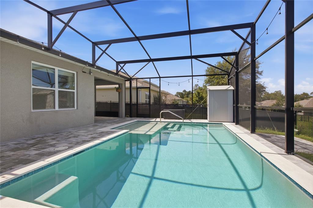 A rectangular swimming pool sits inside a screened-in patio area with light-colored stone pavers — 489 LADY GRACE PLACE, DELAND, FL