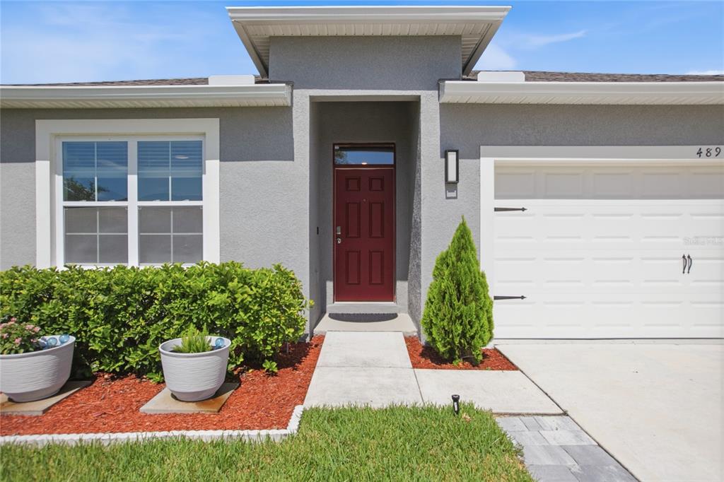 A gray stucco house exterior features a red front door, a garage, and landscaping — 489 LADY GRACE PLACE, DELAND, FL