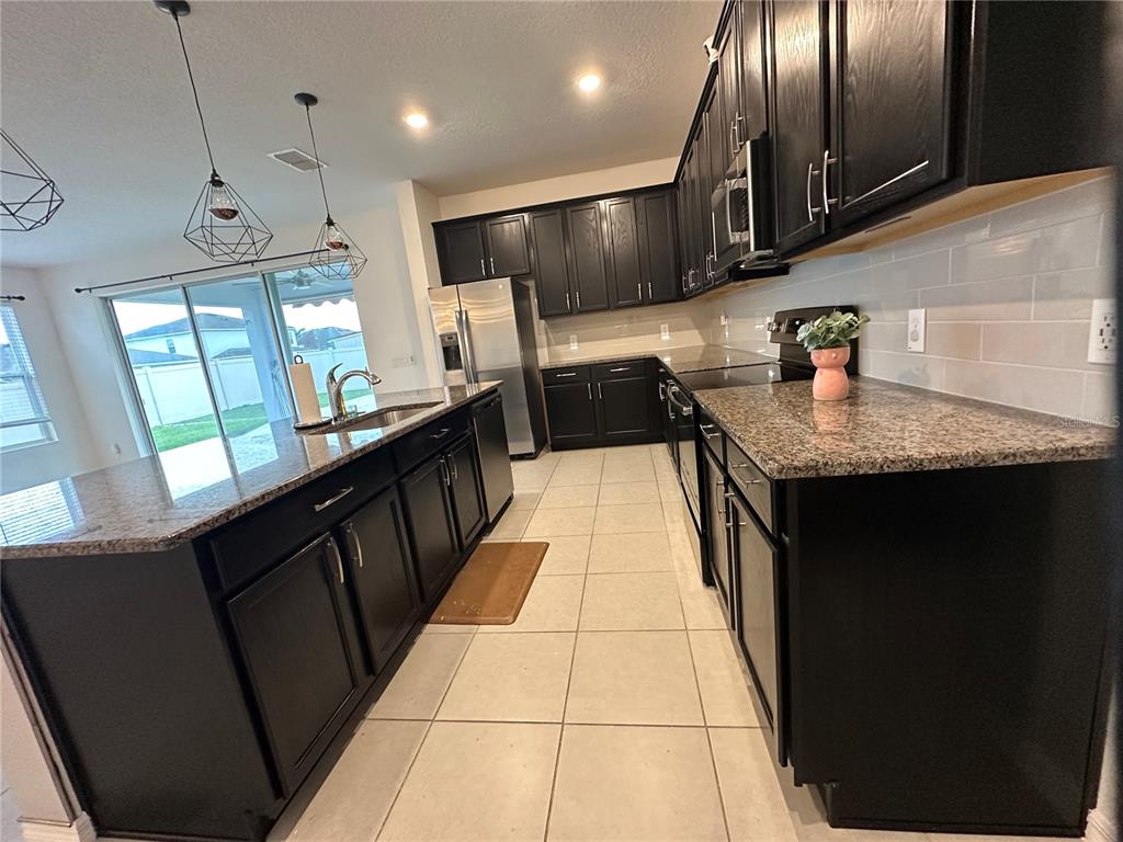 A kitchen features dark cabinets, granite countertops, a large island, and tile flooring — 2104 STILLWOOD WAY, ST CLOUD, FL