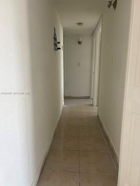A narrow hallway with white walls and light-colored tile flooring leads toward a doorway — 666 W 81st St # 103, Hialeah FL 33014, HIALEAH, FL