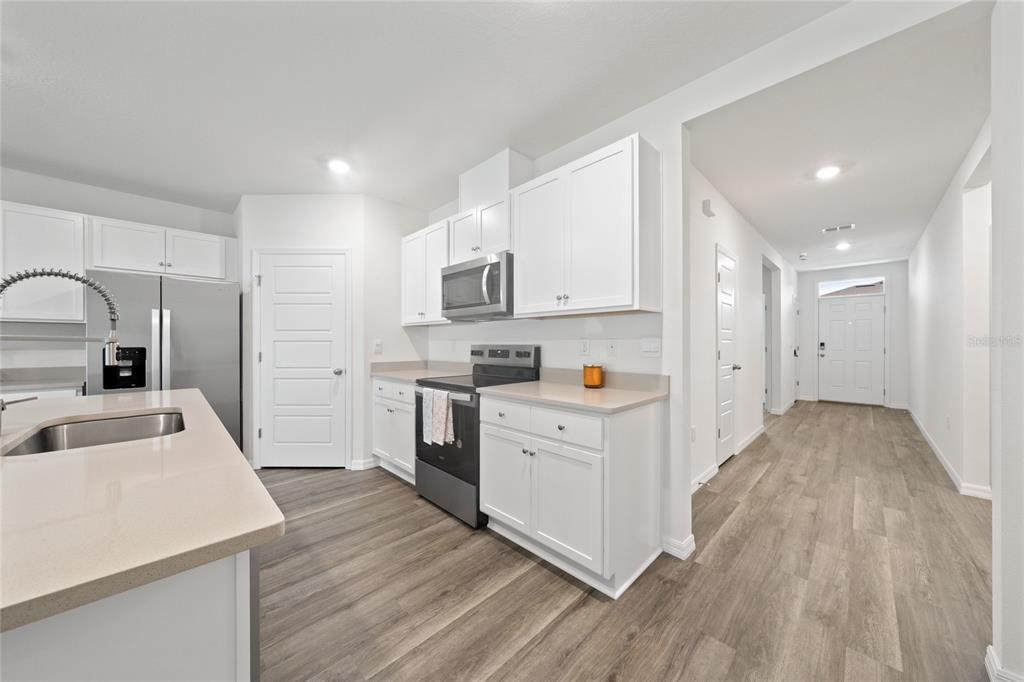 A modern kitchen features white cabinets, stainless steel appliances, and light wood-look flooring — 698 PARK PLACE BOULEVARD, DAVENPORT, FL