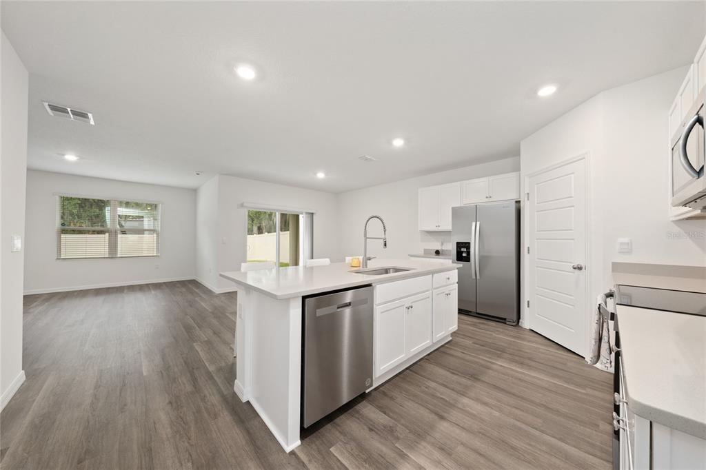 A modern kitchen with white cabinets, stainless steel appliances, and an island overlooks a living area — 698 PARK PLACE BOULEVARD, DAVENPORT, FL