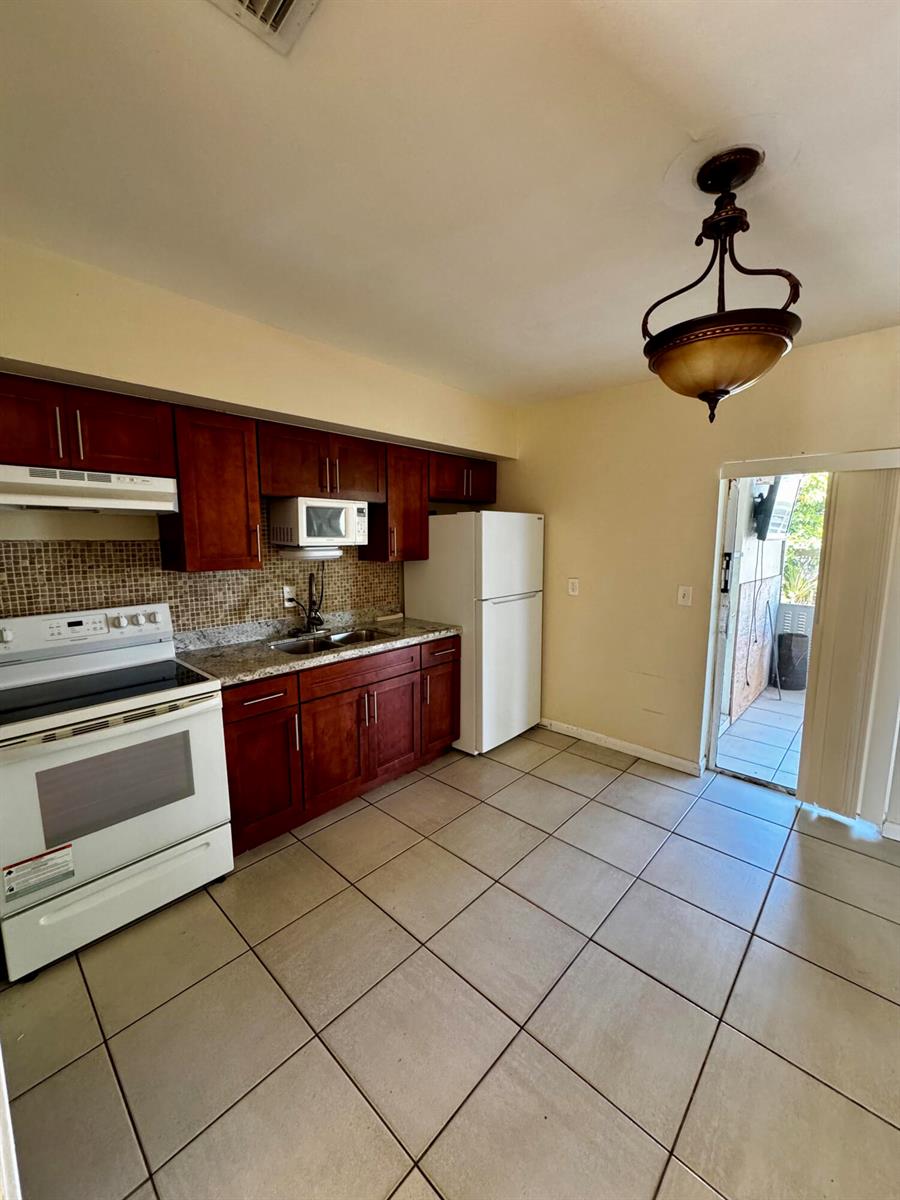 A kitchen with wood cabinets, granite countertops, white appliances, and tile flooring leads to a patio — 2824 N Dixie Highway, Boca Raton FL 33431, BOCA RATON, FL