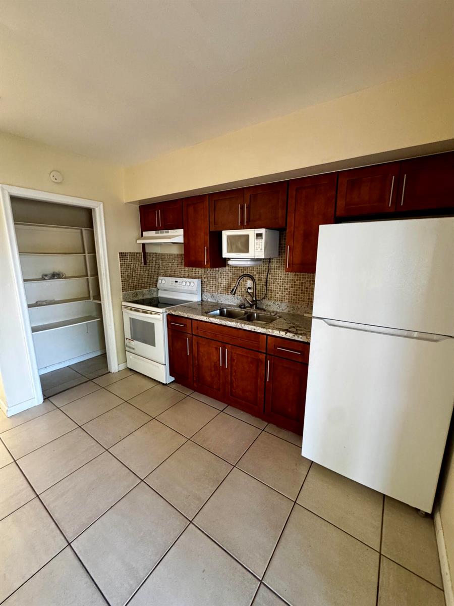 A kitchen features cherry-toned cabinets, white appliances, granite countertops, and a tiled floor — 2824 N Dixie Highway, Boca Raton FL 33431, BOCA RATON, FL