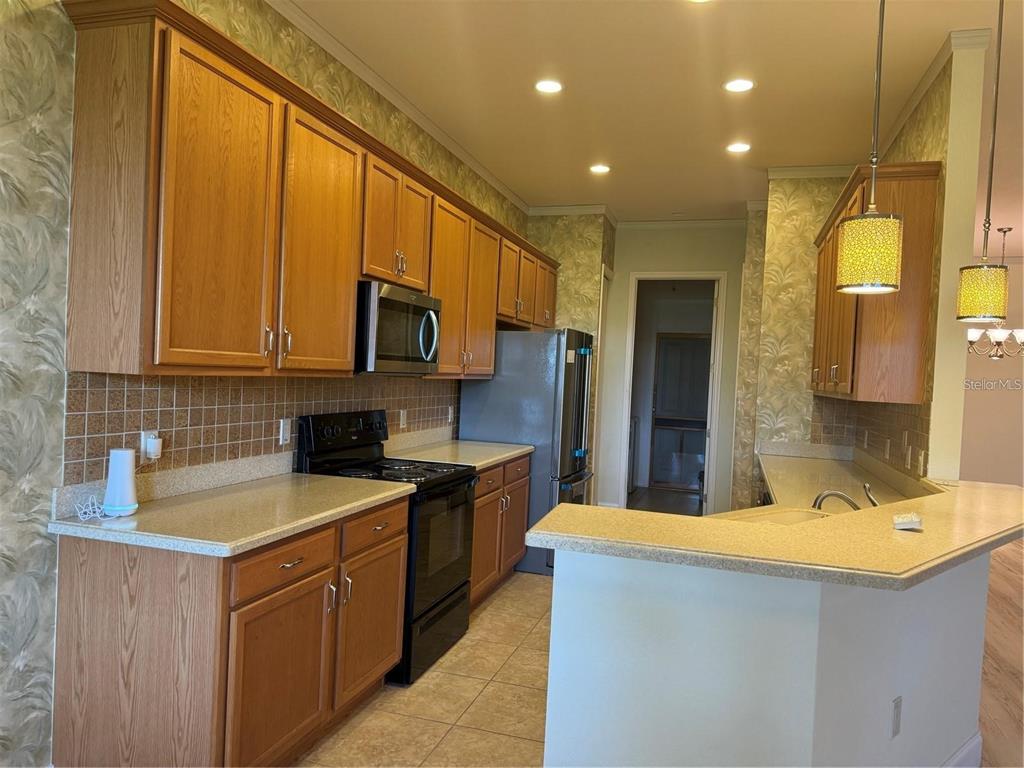 A kitchen features wood cabinets, tan countertops, a tile backsplash, and stainless steel appliances — 2470 SALZBURG LOOP, WINTER HAVEN, FL