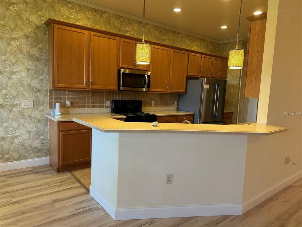 A kitchen features wood cabinets, a breakfast bar, stainless steel appliances, and patterned wallpaper — 2470 SALZBURG LOOP, WINTER HAVEN, FL