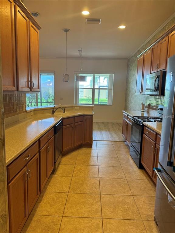 A kitchen features wood cabinets, light countertops, tile flooring, and a view of the outdoors — 2470 SALZBURG LOOP, WINTER HAVEN, FL