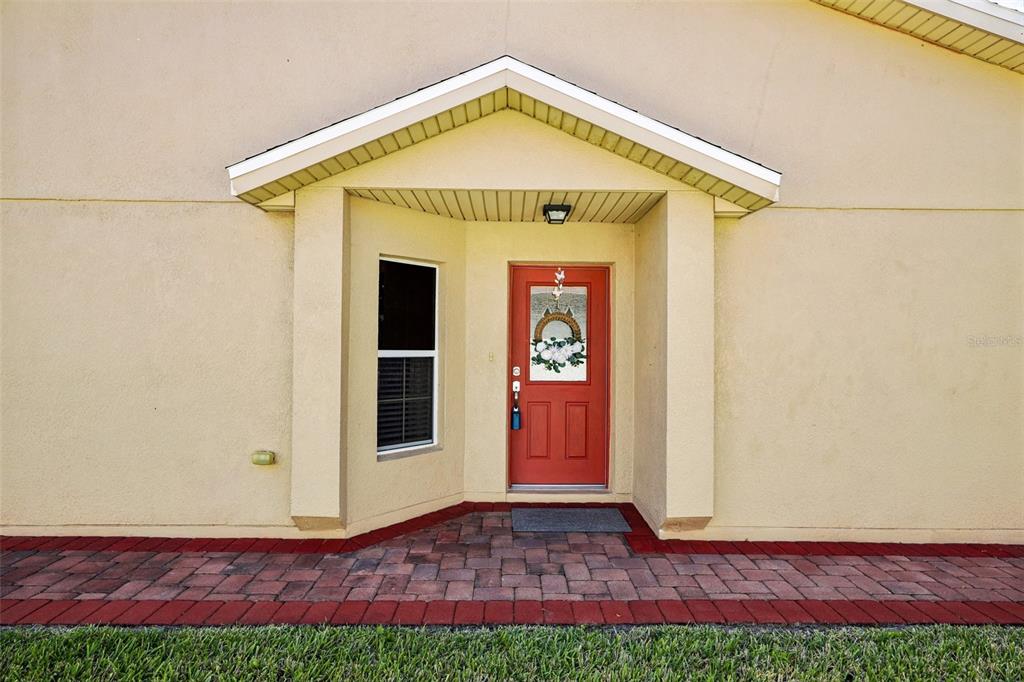 A red front door with a decorative wreath is set within a tan stucco entryway — 516 MILLIFIORA LANE, POINCIANA, FL