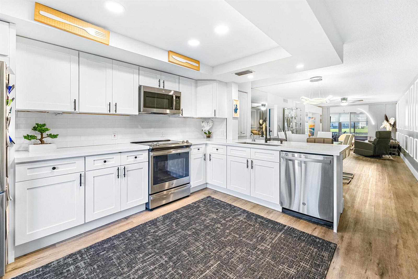 A modern kitchen features white cabinetry, stainless steel appliances, and a dark patterned area rug — 1018 Guildford A, Boca Raton FL 33434, BOCA RATON, FL