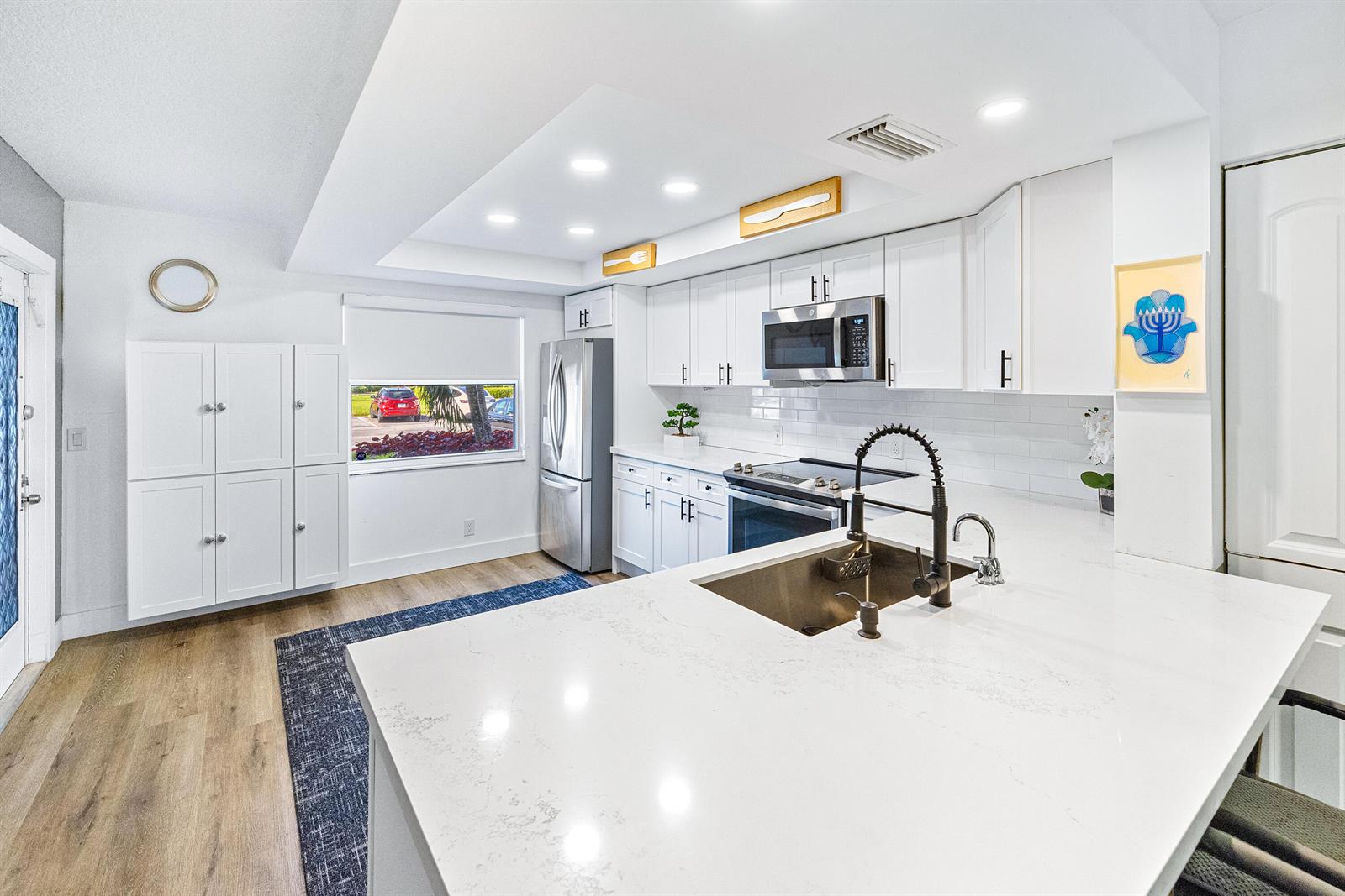 A modern kitchen features white cabinetry, quartz countertops, stainless steel appliances, and a central island — 1018 Guildford A, Boca Raton FL 33434, BOCA RATON, FL