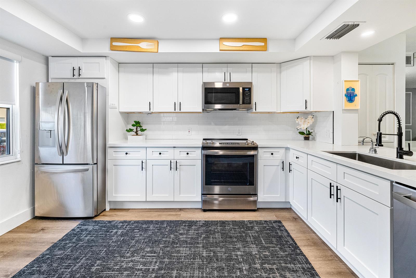 A modern kitchen features white cabinetry, stainless steel appliances, a subway tile backsplash, and wood flooring — 1018 Guildford A, Boca Raton FL 33434, BOCA RATON, FL