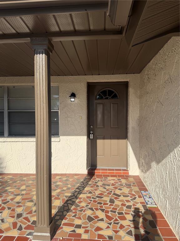 A covered porch with a patterned tile floor leads to a brown front door — 9004 SAINT REGIS LANE, PORT RICHEY, FL