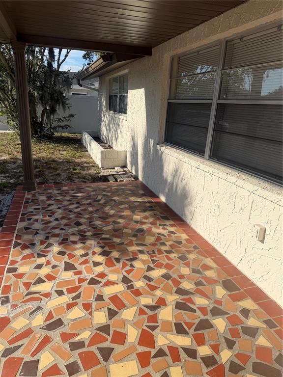 A covered patio features a mosaic tile floor with red, tan, and brown broken pieces — 9004 SAINT REGIS LANE, PORT RICHEY, FL