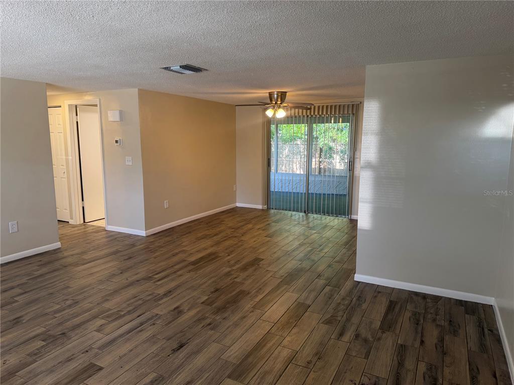 An open living area features wood-look tile flooring, a ceiling fan, and sliding glass doors — 9004 SAINT REGIS LANE, PORT RICHEY, FL