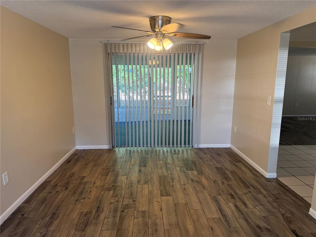 A dining room with wood-look flooring, a ceiling fan, and vertical blinds over sliding doors — 9004 SAINT REGIS LANE, PORT RICHEY, FL