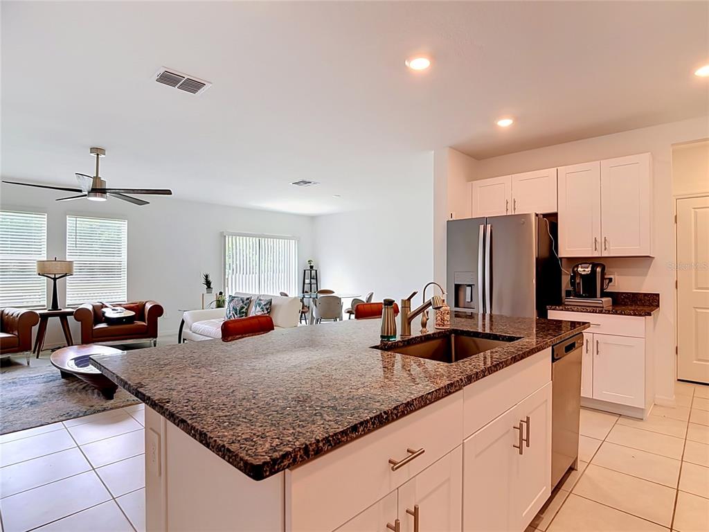 A kitchen island with a granite countertop overlooks an open-concept living and dining area — 1633 RED LOOP, LAKELAND, FL