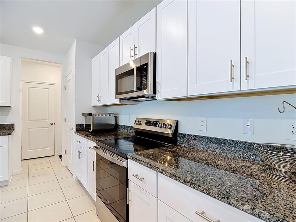 A kitchen features white cabinets, granite countertops, stainless steel appliances, and tile flooring — 1633 RED LOOP, LAKELAND, FL